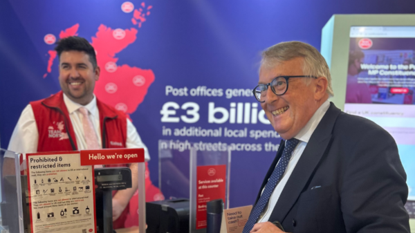 Jamie Stone pictured as a Post Office counter smiling with a staff member